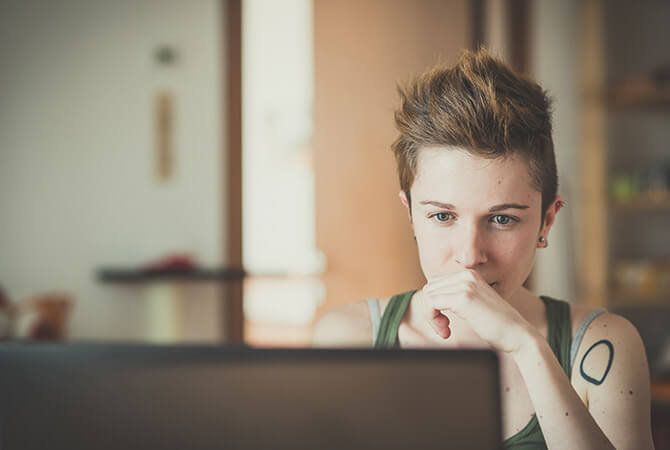 short-haired lady with arm tattoo looking contemplatively at computer screen