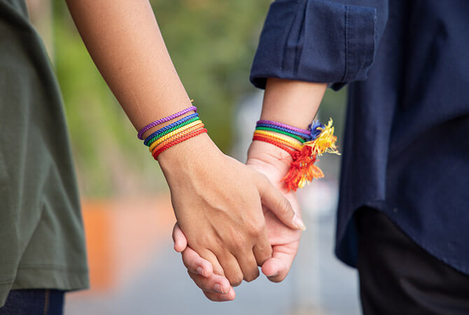 two people wearing rainbow bracelets holding hands